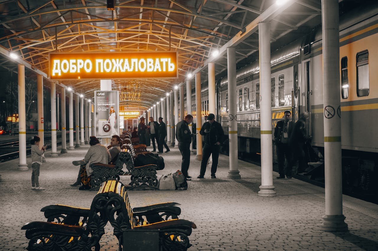 Passengers wait at Tashkent railway station under a neon welcome sign.