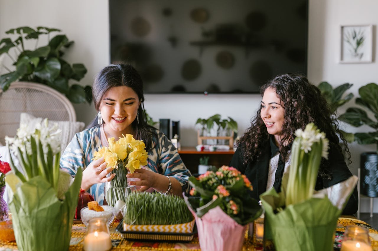 Two women celebrating Nowruz with flowers and traditional decorations indoors.